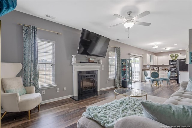4943 Lion Heart Ln, Parkton, NC 28371 - living area featuring ceiling fan, dark wood-style floors, a fireplace with raised hearth, and baseboards
