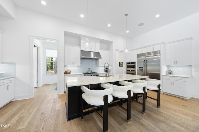 7545 Hasentree Club Dr, Wake Forest, NC 27587 - kitchen featuring appliances with stainless steel finishes, under cabinet range hood, tasteful backsplash, a center island with sink, and a breakfast bar