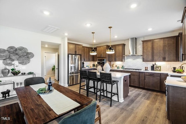1021 Dillon Lake Dr, Knightdale, NC 27545 - kitchen featuring wall chimney exhaust hood, appliances with stainless steel finishes, a kitchen island, a breakfast bar area, and light countertops