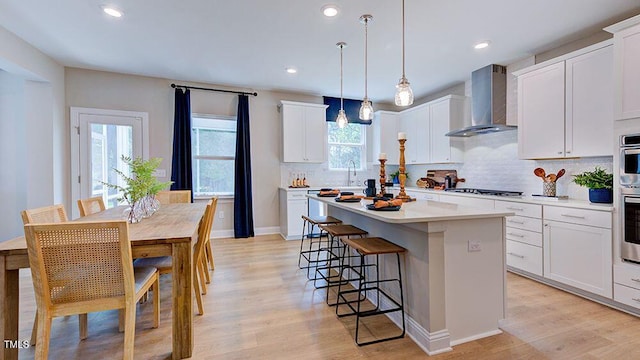 1021 Dillon Lake Dr, Knightdale, NC 27545 - kitchen with wall chimney range hood, a center island, tasteful backsplash, light wood-style floors, and white cabinets
