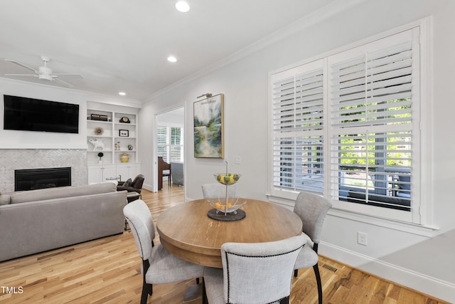 911 Canterbury Rd, Raleigh, NC 27607 - dining space featuring crown molding, baseboards, light wood-style floors, ceiling fan, and a glass covered fireplace