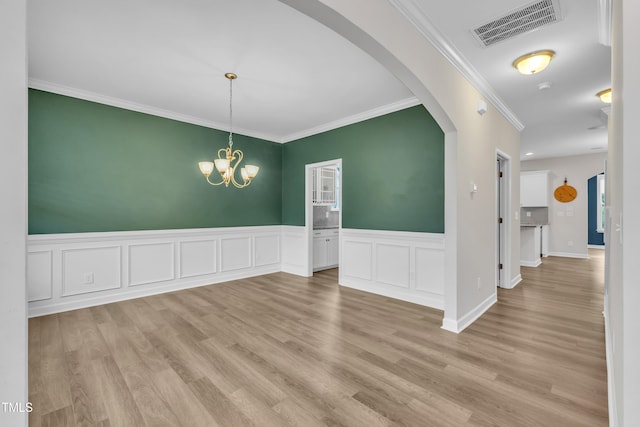 3449 S Beaver Ln, Raleigh, NC 27604 - unfurnished dining area featuring arched walkways, light wood-type flooring, ornamental molding, a wainscoted wall, and a chandelier
