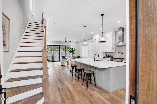 606 Velma Hopkins Ln, Raleigh, NC 27603 - kitchen with wall chimney range hood, white cabinets, backsplash, a breakfast bar area, and light wood finished floors