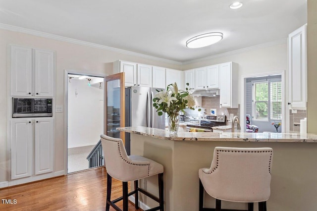 4329 Hawksong Pl, Cary, NC 27518 - kitchen with under cabinet range hood, stainless steel range with electric cooktop, a kitchen bar, backsplash, and ornamental molding