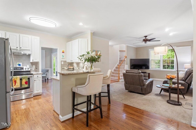 4329 Hawksong Pl, Cary, NC 27518 - kitchen with stainless steel appliances, open floor plan, a breakfast bar, white cabinetry, and ornamental molding