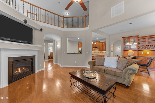 7768 Berry Crest Ave, Raleigh, NC 27617 - living area featuring arched walkways, a ceiling fan, light wood finished floors, a glass covered fireplace, and baseboards