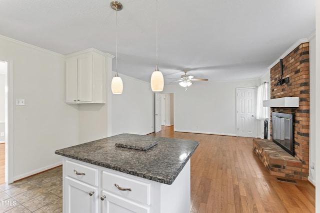 6411 Pondview Ln, Durham, NC 27712 - kitchen with a ceiling fan, baseboards, a brick fireplace, white cabinets, and light wood-type flooring