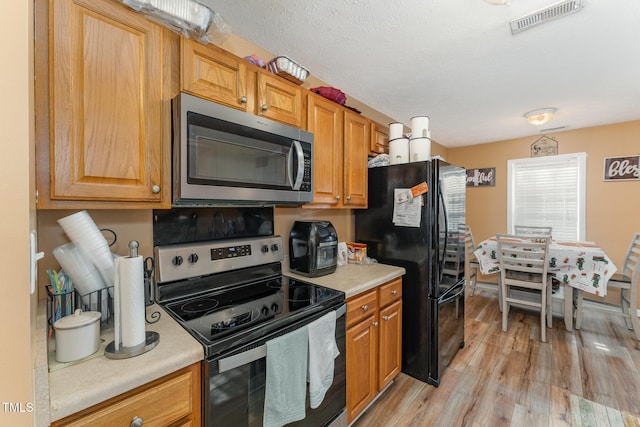 1515 Mack St, Spring Lake, NC 28390 - kitchen featuring appliances with stainless steel finishes, light countertops, light wood-type flooring, brown cabinets, and a textured ceiling