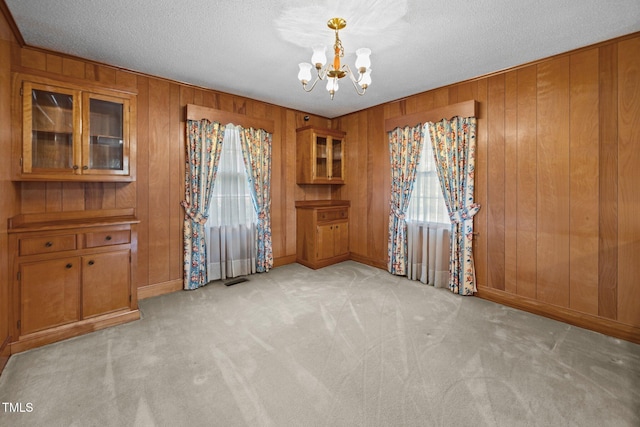 4804 Spring Forest Rd, Raleigh, NC 27616 - unfurnished dining area featuring a chandelier, light colored carpet, wood walls, and a textured ceiling