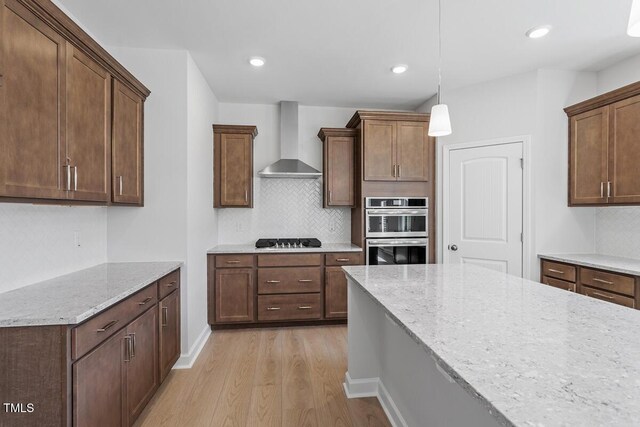 257 N Maple Walk Dr Unit 218, Garner, NC 27529 - kitchen featuring wall chimney exhaust hood, stainless steel double oven, light wood-style floors, cooktop, and backsplash