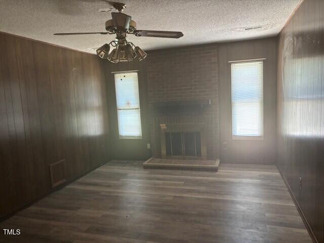 708 Old Barn Ave, Durham, NC 27704 - unfurnished living room featuring wooden walls, a ceiling fan, a textured ceiling, wood finished floors, and healthy amount of natural light