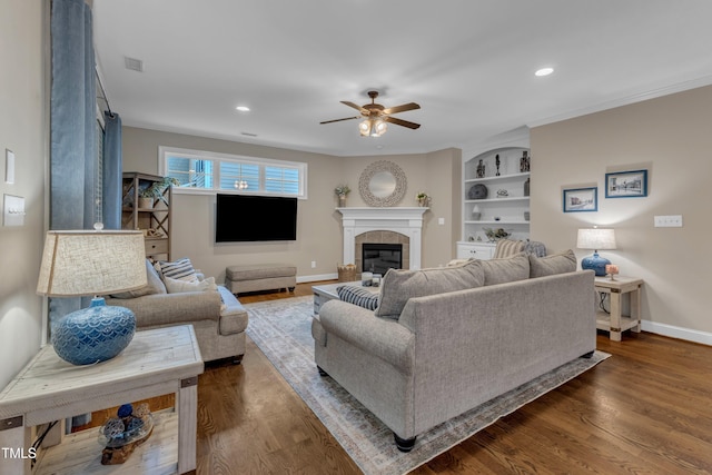 3111 Virginia Pine Ln, Apex, NC 27539 - living room featuring a ceiling fan, a tiled fireplace, dark wood-type flooring, ornamental molding, and built in shelves