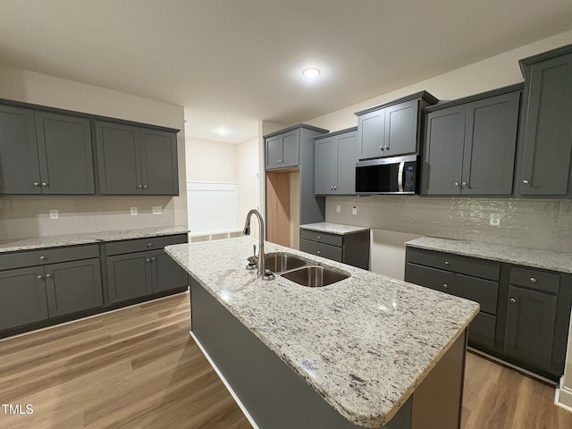 78 Mineral Springs Way, Benson, NC 27504 - kitchen with stainless steel microwave, light wood-style flooring, light stone counters, an island with sink, and tasteful backsplash