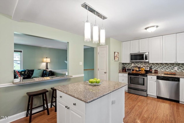 1109 Buckingham Rd, Garner, NC 27529 - kitchen with appliances with stainless steel finishes, decorative backsplash, light wood-style flooring, white cabinetry, and pendant lighting