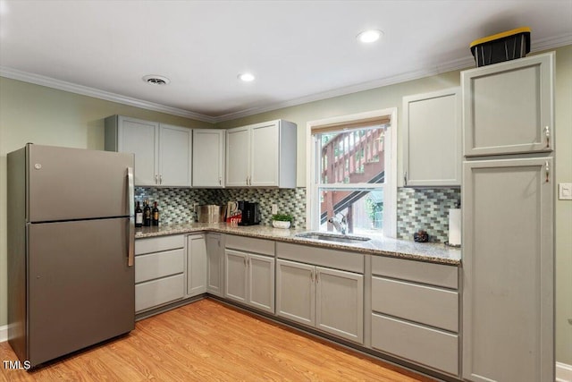 1109 Buckingham Rd, Garner, NC 27529 - kitchen with freestanding refrigerator, light wood-style flooring, decorative backsplash, light stone counters, and crown molding