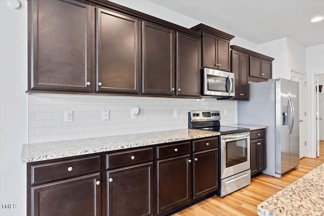 346 E Painted Way, Clayton, NC 27527 - kitchen featuring appliances with stainless steel finishes, light wood-style floors, dark brown cabinetry, tasteful backsplash, and light stone counters