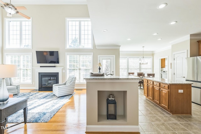 30155 Pharr, Chapel Hill, NC 27517 - kitchen with freestanding refrigerator, an island with sink, brown cabinetry, crown molding, and light stone countertops