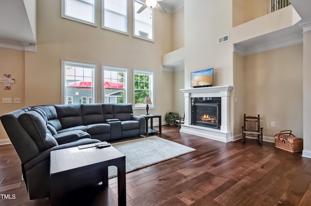 2100 Della Ct, Apex, NC 27502 - living room featuring a ceiling fan, a glass covered fireplace, dark wood-style floors, a towering ceiling, and ornamental molding