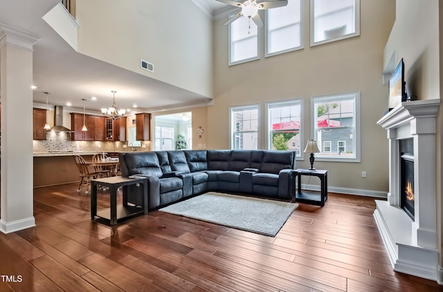 2100 Della Ct, Apex, NC 27502 - living room featuring a ceiling fan, a lit fireplace, crown molding, dark wood-style floors, and a towering ceiling