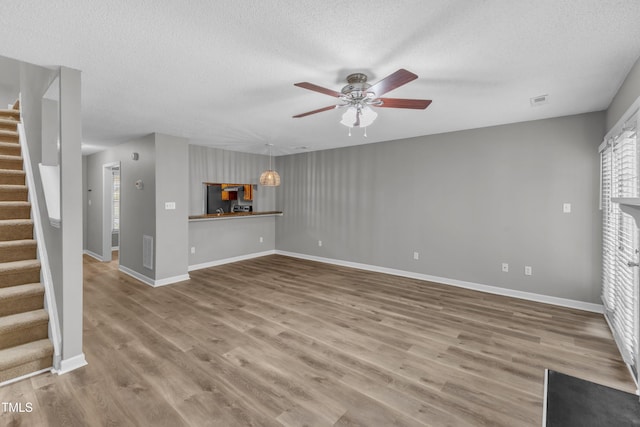 4658 Fawnbrook Cir, Raleigh, NC 27612 - unfurnished living room featuring stairway, a textured ceiling, a ceiling fan, wood finished floors, and baseboards