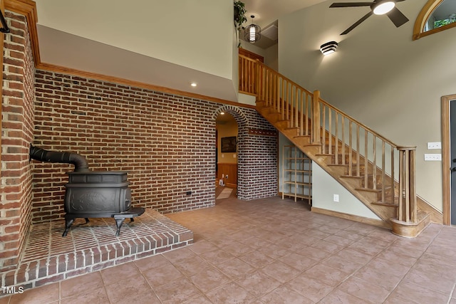 145 Ryan Rd, Pittsboro, NC 27312 - tiled living room featuring a wood stove, a towering ceiling, ceiling fan, stairway, and brick wall