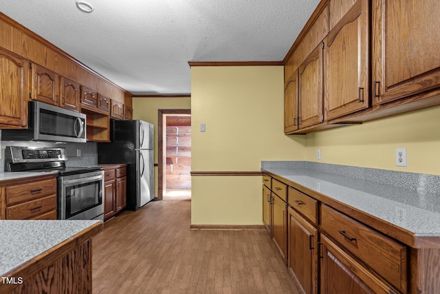 5437 Grasshopper Rd, Raleigh, NC 27610 - kitchen featuring appliances with stainless steel finishes, wood finished floors, crown molding, brown cabinets, and a textured ceiling