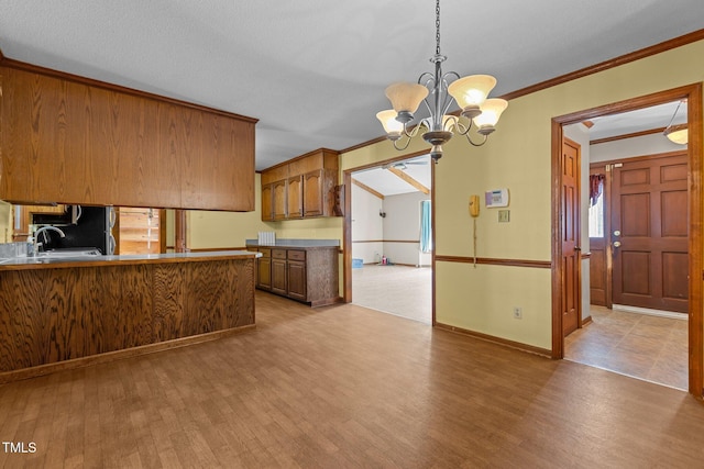 5437 Grasshopper Rd, Raleigh, NC 27610 - kitchen featuring wood finished floors, a chandelier, brown cabinets, ornamental molding, and hanging light fixtures