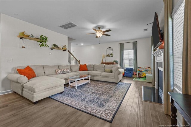 453 Falls Creek Dr, Spring Lake, NC 28390 - living room featuring wood finished floors, a ceiling fan, a fireplace with flush hearth, and stairway