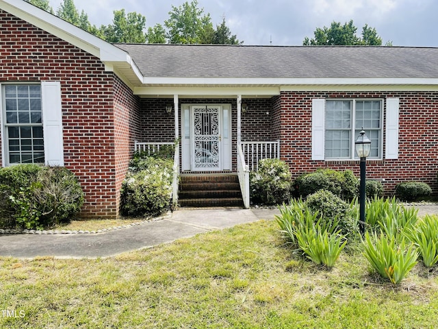 65 Opie Frazier Rd, Henderson, NC 27537 - property entrance featuring brick siding, a yard, a shingled roof, and covered porch