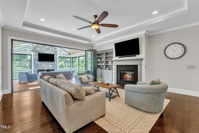 1716 Arberdour Dr, Apex, NC 27502 - living area featuring a glass covered fireplace, a tray ceiling, ceiling fan, wood-type flooring, and crown molding
