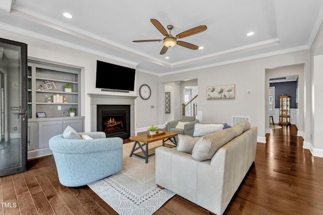 1716 Arberdour Dr, Apex, NC 27502 - living room featuring dark wood-type flooring, ceiling fan, a warm lit fireplace, a raised ceiling, and ornamental molding