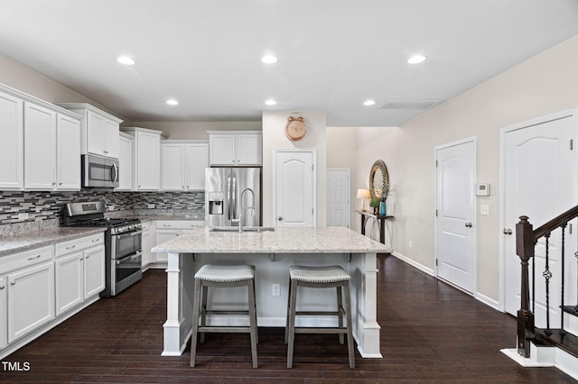 105 Putters Ct, Durham, NC 27703 - kitchen with stainless steel appliances, a kitchen breakfast bar, white cabinetry, dark wood finished floors, and decorative backsplash