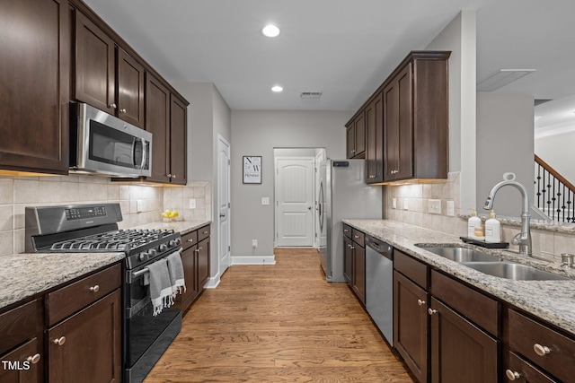 238 Langford Valley Way, Cary, NC 27513 - kitchen with appliances with stainless steel finishes, a sink, dark brown cabinetry, light wood-type flooring, and light stone counters