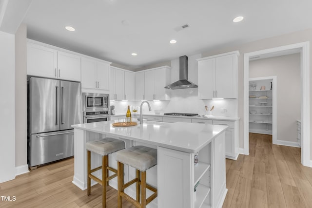 109 Crested Coral Dr, Holly Springs, NC 27540 - kitchen featuring stainless steel appliances, wall chimney exhaust hood, light countertops, a kitchen breakfast bar, and light wood-style floors