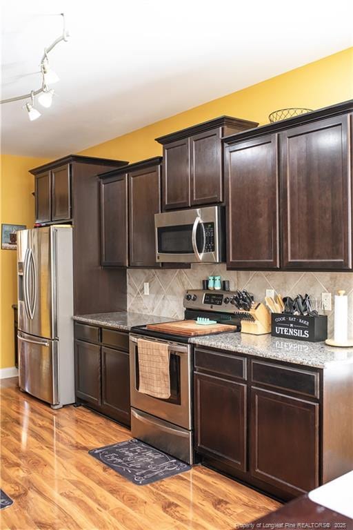 101 Birdsong Ct, Aberdeen, NC 28315 - kitchen with stainless steel appliances, dark brown cabinets, light wood-type flooring, light stone countertops, and decorative backsplash