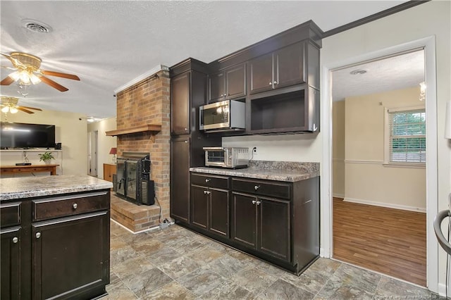 2547 Red Springs Rd, Raeford, NC 28376 - kitchen featuring stainless steel microwave, a ceiling fan, a fireplace, a textured ceiling, and dark brown cabinets