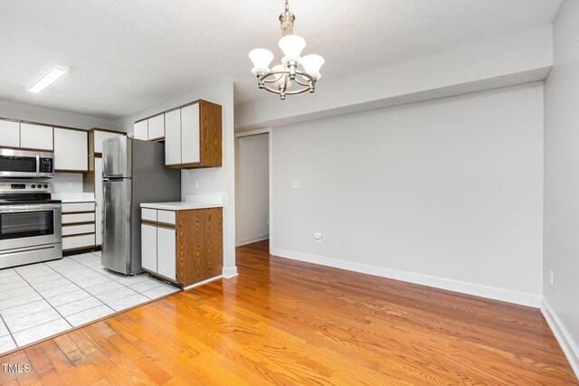 3306 Woodland Park Rd, Durham, NC 27703 - kitchen featuring stainless steel appliances, a chandelier, white cabinetry, light countertops, and light wood-type flooring