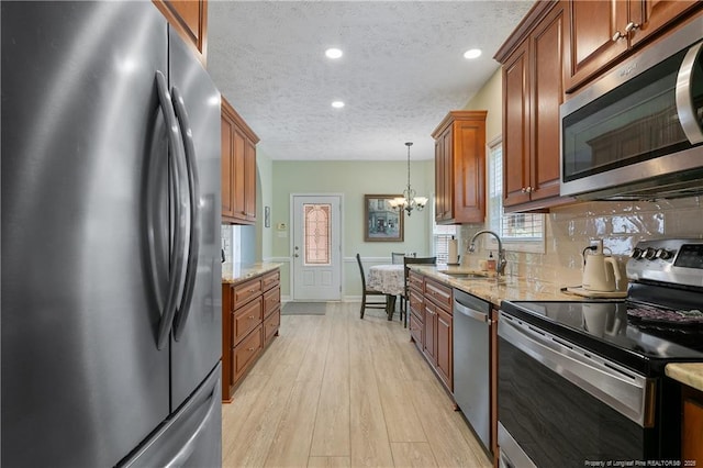 5387 Clubhouse Ln, Hope Mills, NC 28348 - kitchen with stainless steel appliances, a sink, brown cabinetry, a textured ceiling, and light wood-style flooring
