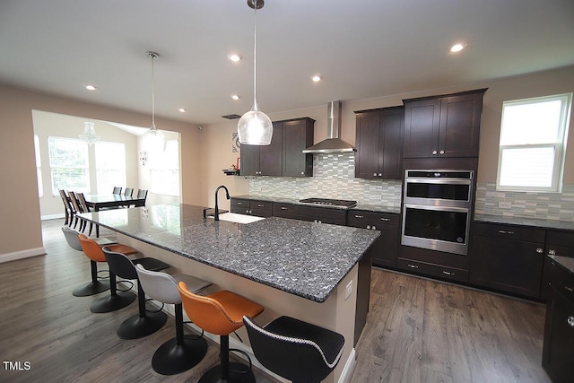 4416 Walker Hallow St, Raleigh, NC 27616 - kitchen featuring wall chimney range hood, stainless steel appliances, a breakfast bar area, decorative backsplash, and dark wood-style flooring