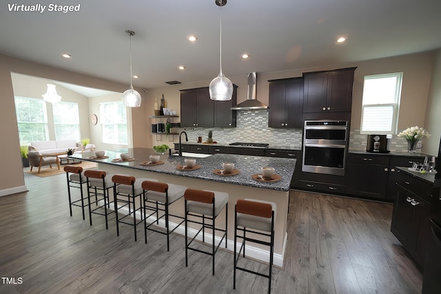4416 Walker Hallow St, Raleigh, NC 27616 - kitchen featuring wall chimney range hood, gas cooktop, stainless steel double oven, a breakfast bar, and tasteful backsplash