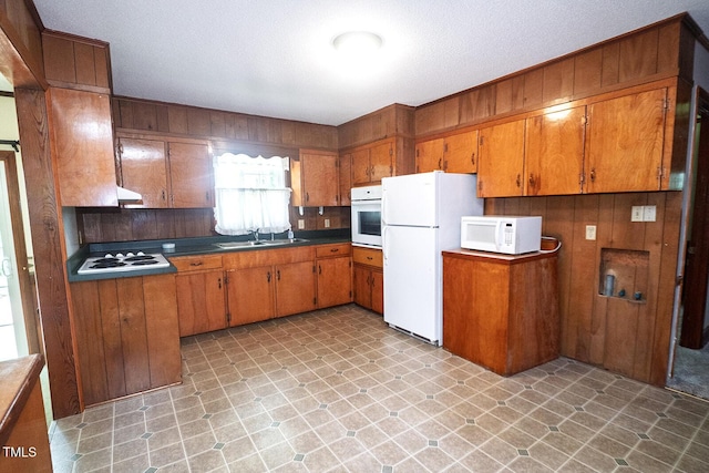 205 N Augusta Ave, Benson, NC 27504 - kitchen with white appliances, brown cabinets, wood walls, a sink, and under cabinet range hood