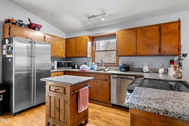 501 Enon Rd, Oxford, NC 27565 - kitchen featuring appliances with stainless steel finishes, light wood finished floors, brown cabinetry, a center island, and a textured ceiling