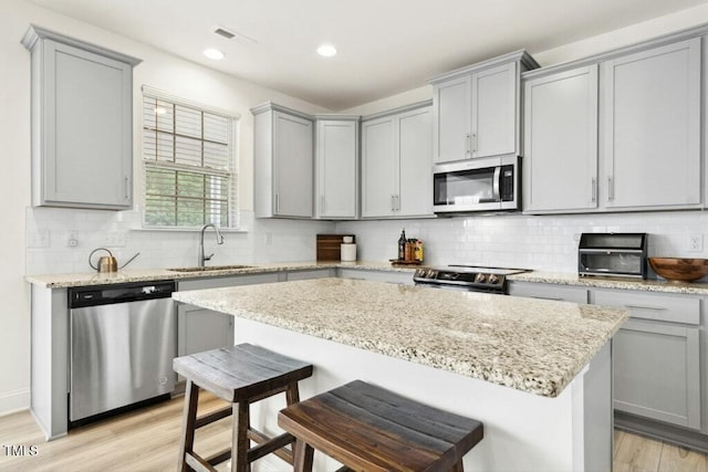 116 Hayfield Dr, Lillington, NC 27546 - kitchen featuring appliances with stainless steel finishes, gray cabinetry, a sink, a breakfast bar area, and light wood finished floors