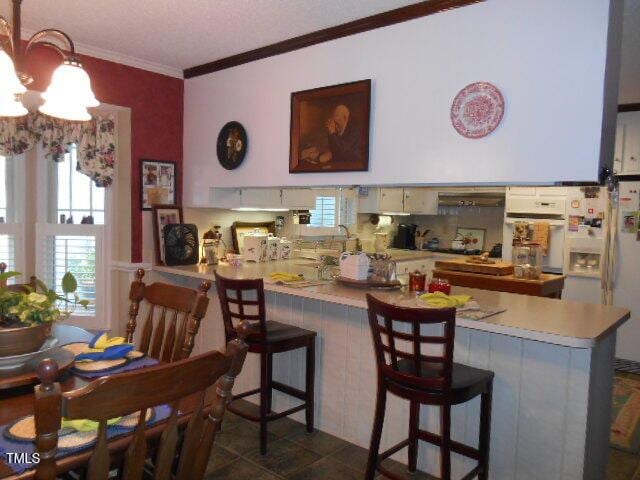6517 Whitted Rd, Fuquay Varina, NC 27526 - kitchen featuring a chandelier, white appliances, crown molding, a peninsula, and a breakfast bar area