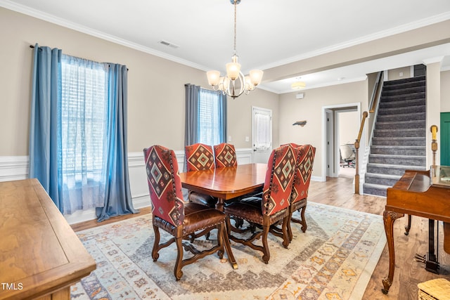 137 Clydes Point Way, Wendell, NC 27591 - dining space with a chandelier, stairs, crown molding, light wood-style flooring, and a wainscoted wall
