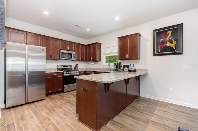 150 Sherrill Place Ln, Garner, NC 27529 - kitchen featuring stainless steel appliances, a peninsula, light wood-style floors, a breakfast bar, and light stone countertops