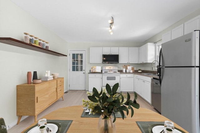 4021 Chaucer Dr, Durham, NC 27705 - kitchen featuring appliances with stainless steel finishes, a sink, white cabinets, light wood-style floors, and open shelves