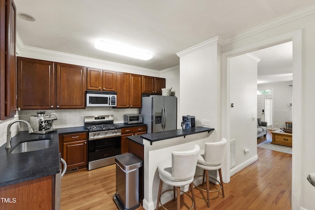 222 Ashton Hall Ln, Raleigh, NC 27609 - kitchen with stainless steel appliances, a sink, light wood finished floors, dark countertops, and a kitchen breakfast bar