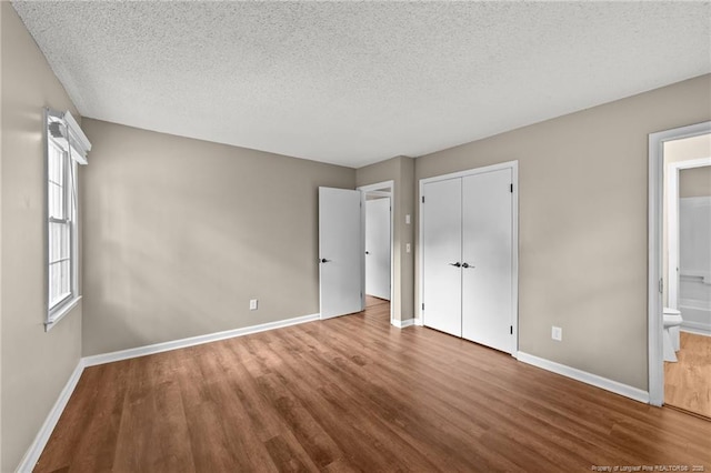 2308 Keith Dr, Raleigh, NC 27610 - unfurnished bedroom with wood finished floors, baseboards, a textured ceiling, a closet, and connected bathroom