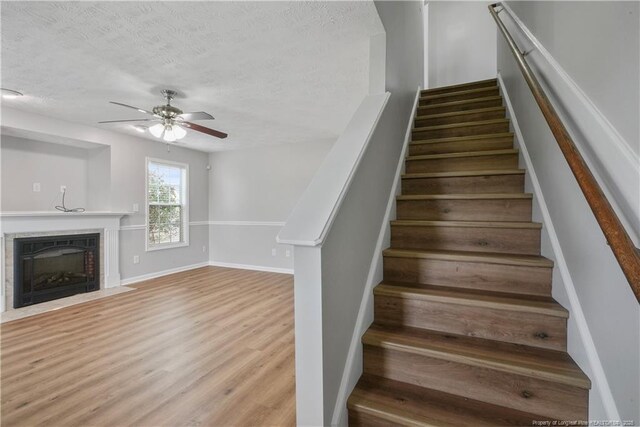 153 Abbey Ln, Raeford, NC 28376 - staircase with ceiling fan, a textured ceiling, wood finished floors, a fireplace with flush hearth, and baseboards
